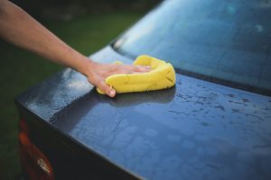 hand washing back of car with large yellow sponge, water droplets visible on car paint