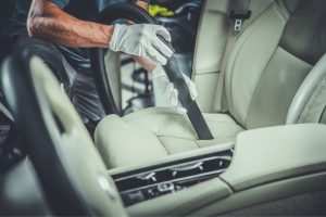 gloved hands using vacuum attachment to clean a vehicle's front passenger seat