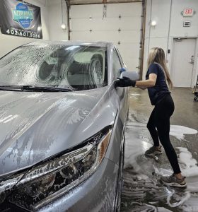 Young woman hand washing a car at the Nebraska Auto Detail shop.